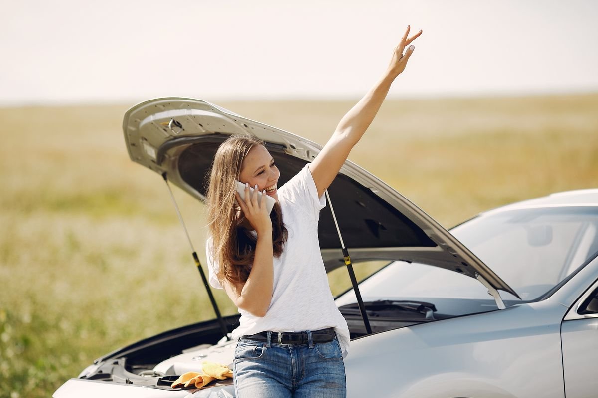 Driver standing by a broken-down car with the hood open, calling for roadside assistance