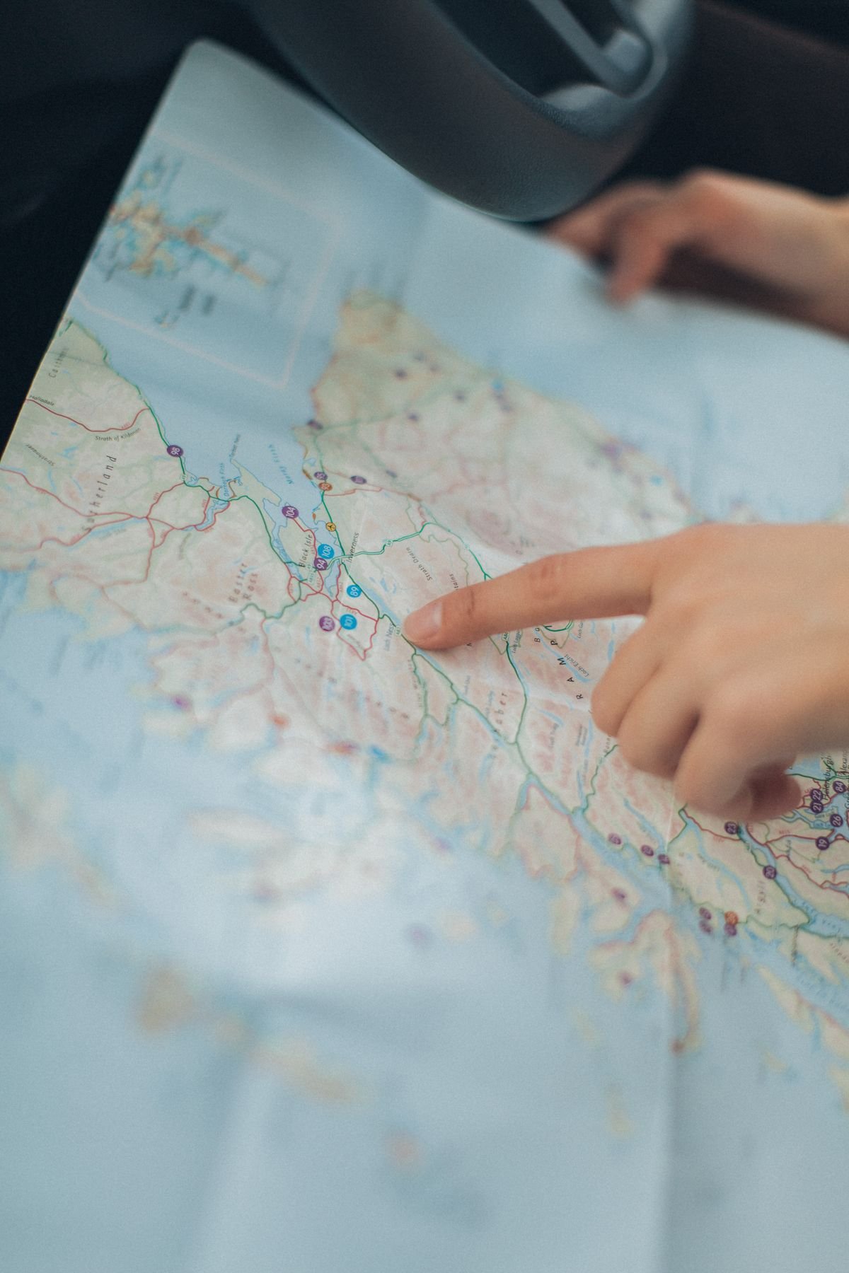 Hand pointing at a location on a map while planning a road trip inside a vehicle