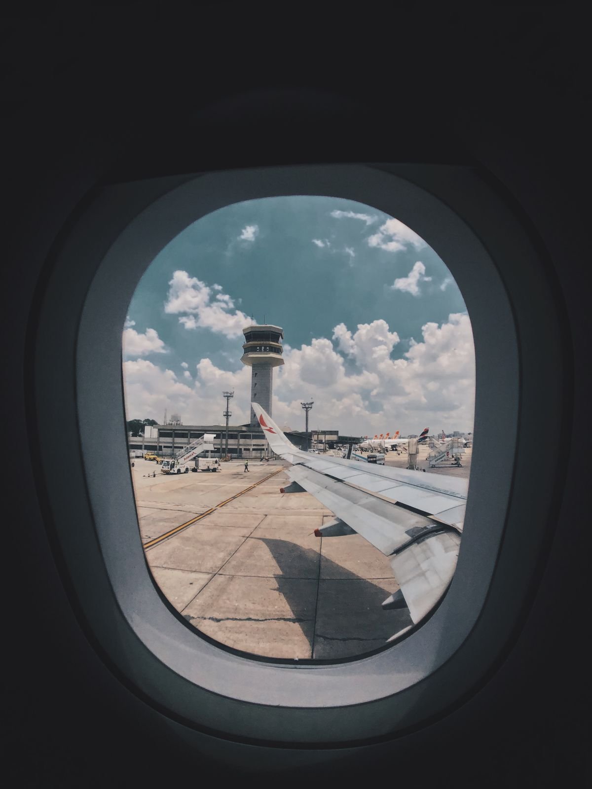 Airplane wing view through the window showing airport control tower and tarmac