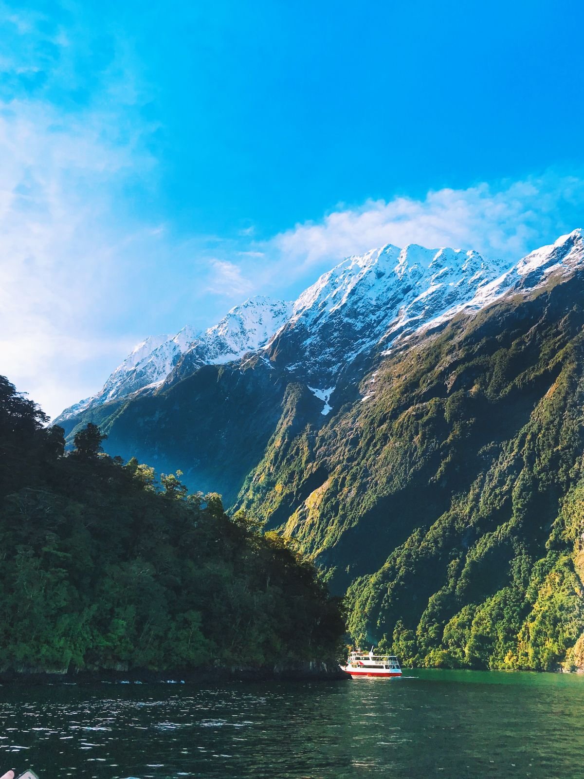 Boat sailing through Milford Sound with snow-capped mountains in New Zealand