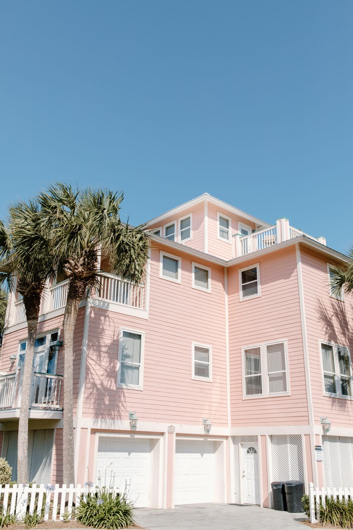 Pastel pink beach house vacation rental with palm trees against a clear blue sky
