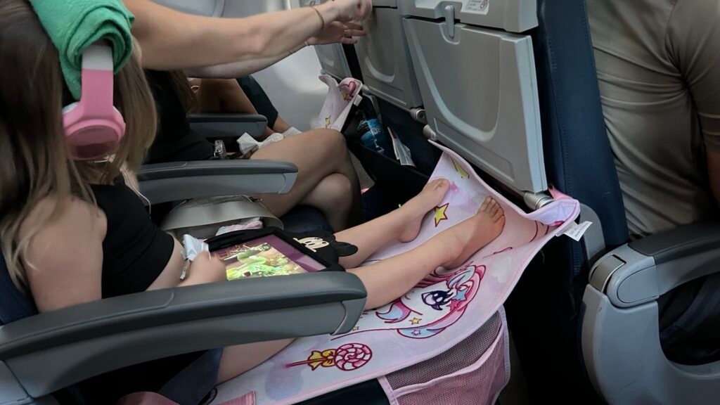 Toddler using an airplane seat-back footrest and tablet during a flight